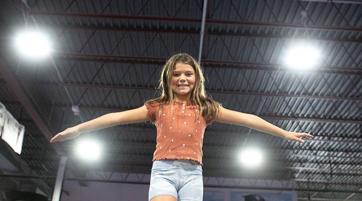 A smiling young gymnast balancing on the beam with her arms out